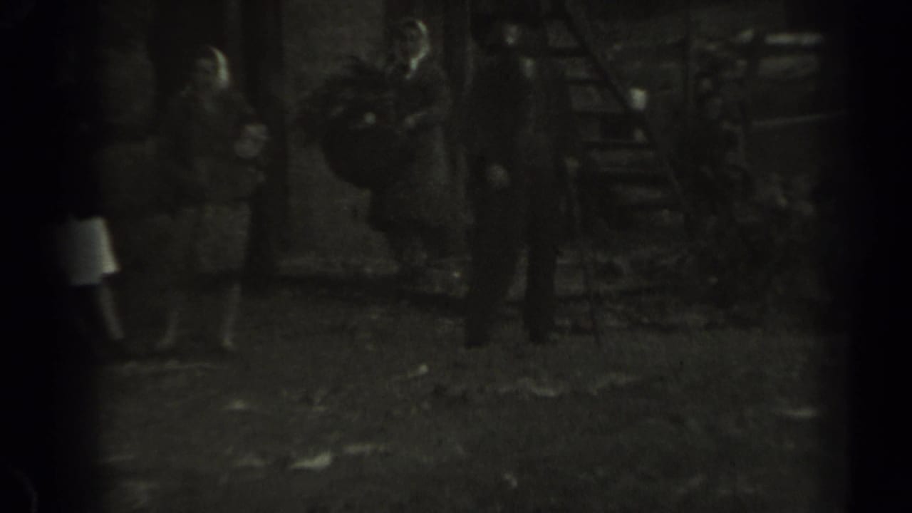 Adults gather near a wooden stair or platform in grainy 1961 Missouri 8mm footage.