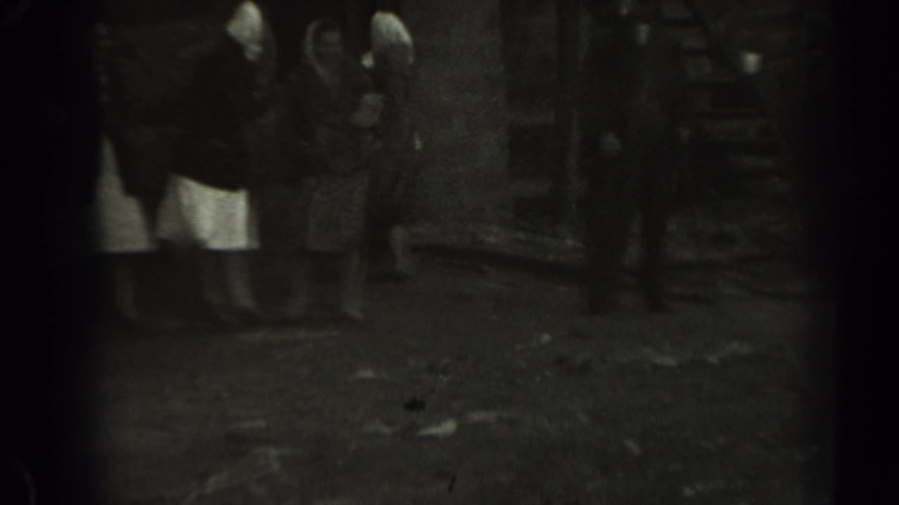 Women in dresses and head coverings stand near a wooden structure in rural Missouri home-movie footage.