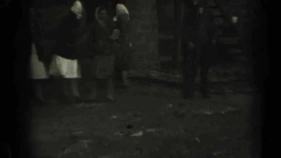 Women in dresses and head coverings stand near a wooden structure in rural Missouri home-movie footage.
