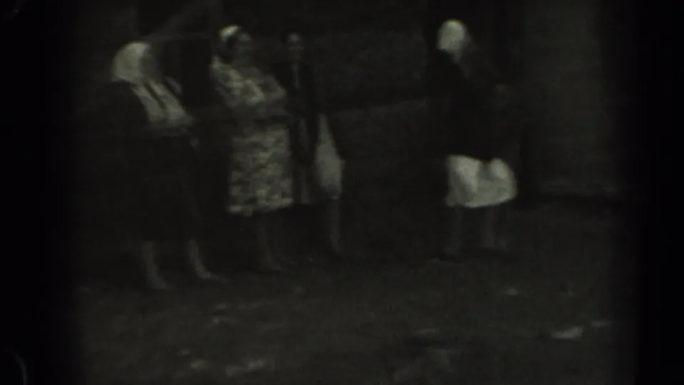 A small group of women stands together near a wooden structure in 1961 rural Missouri footage.