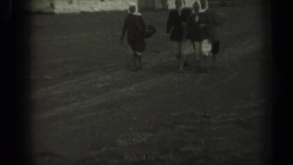 In 1961 Missouri home-movie footage, three older women in headscarves and skirts walk across a dirt field.