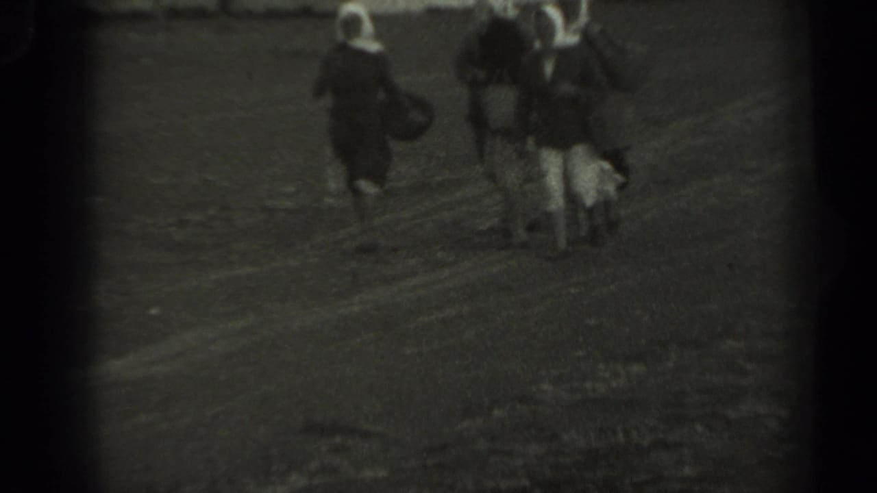 1961 Missouri 8mm frame showing three women in dark dresses and white head coverings walking together on an unpaved path.