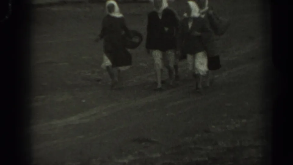 1961 Missouri home-movie frame of three women in dresses and white head coverings approaching along a rough outdoor path.