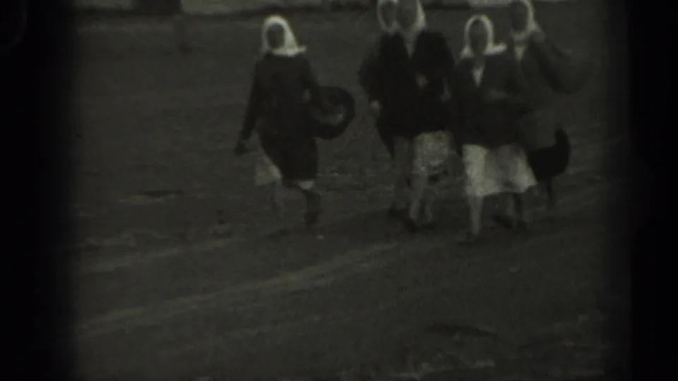 Grainy 1961 Missouri 8mm frame showing women in period dress walking on a rural path with carried bags.