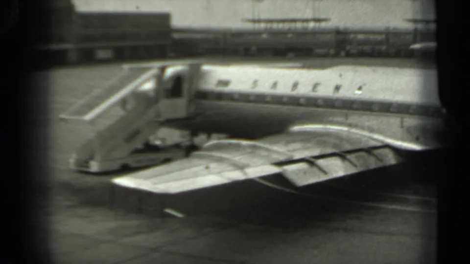 1961 Missouri airport view from near an aircraft wing, looking toward a Sabena fuselage, mobile stairs, and terminal-side structures.