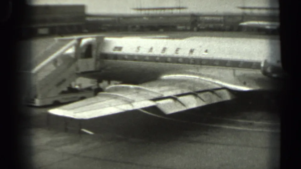 1961 Missouri 8mm frame showing a Sabena passenger aircraft parked on the tarmac, viewed past the wing from a low angle.