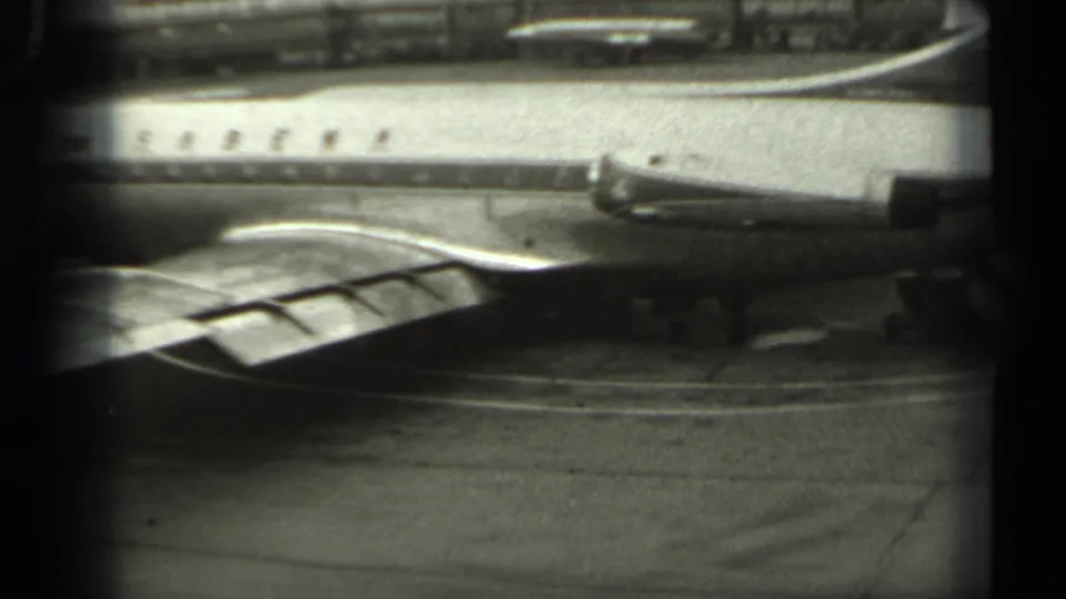 Sabena-branded passenger aircraft seen in black-and-white 8mm footage, with the wing area and airport pavement visible.
