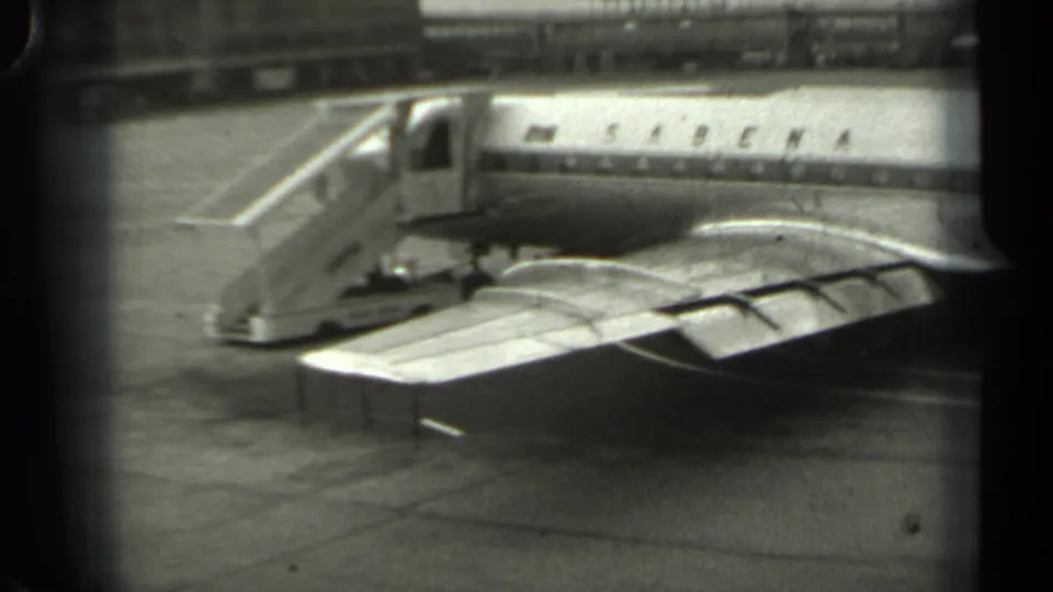 1961 Missouri home-movie frame showing a Sabena passenger airplane on an airport tarmac with boarding stairs nearby.
