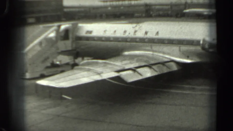 A black-and-white 8mm view of a Sabena airplane on a Missouri airport tarmac, partially obscured by window framing.