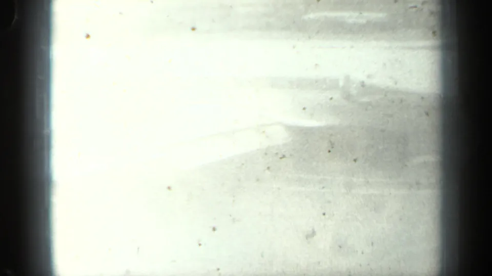 Overexposed 8mm frame from the same airport clip, with only faint pavement and film texture visible.
