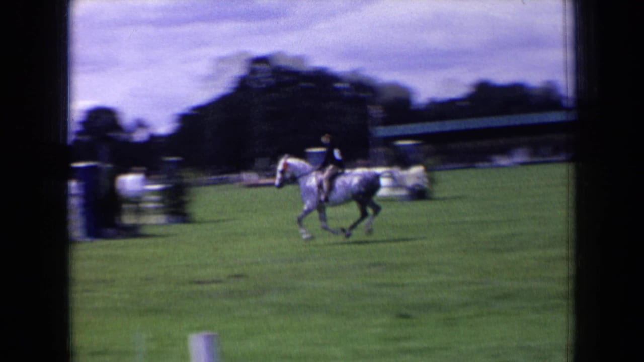 Rider on a dapple gray horse galloping across a grassy show field.