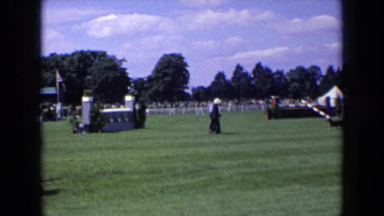 Man continues across the lawn near white fencing, trees, a tent, and event equipment.