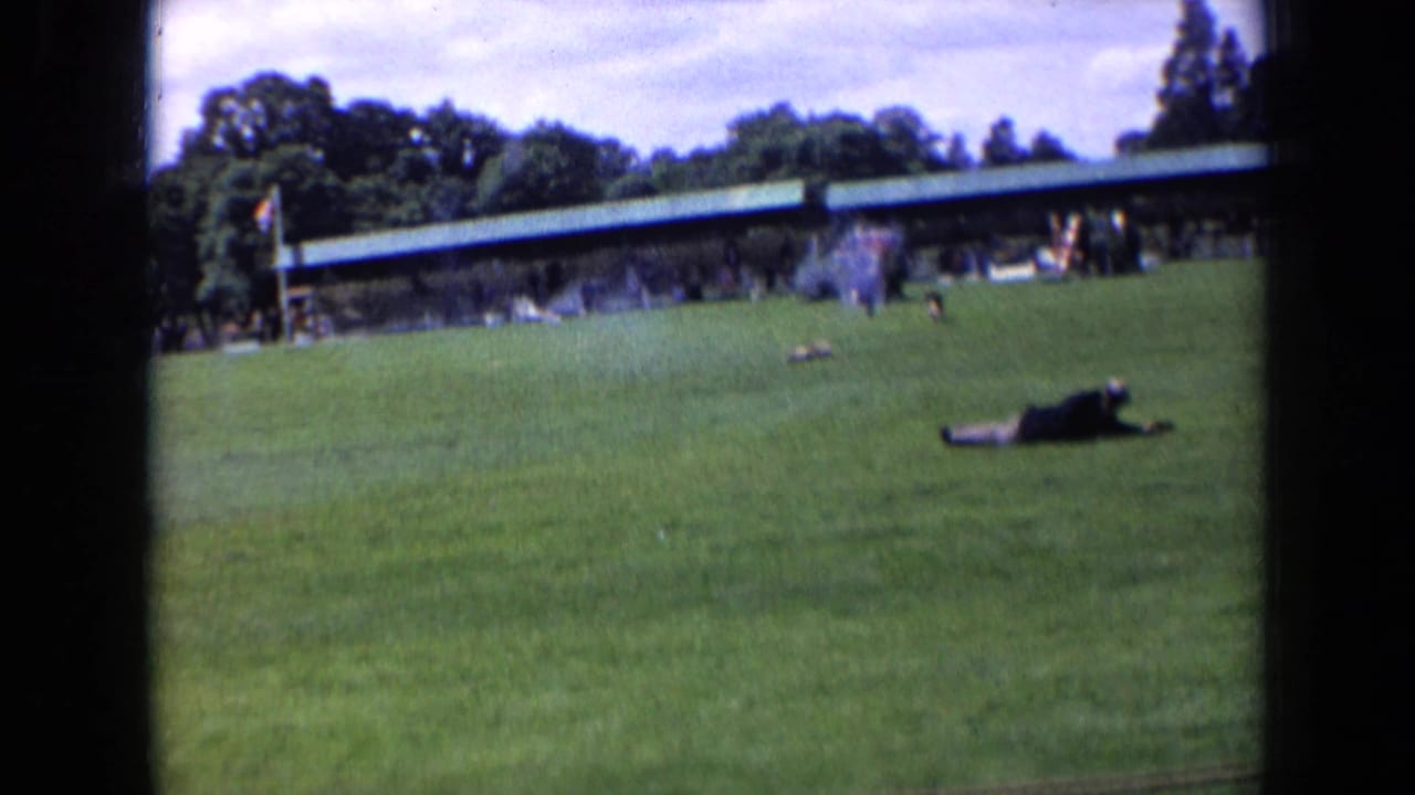 Wide 8mm frame from England in 1963 showing a dog on a public sports pitch near a person on the ground.
