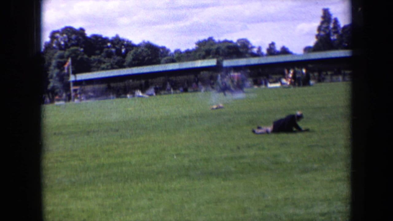 Final 1963 England home-movie frame showing the dog farther across the pitch, with a covered spectator line behind it.