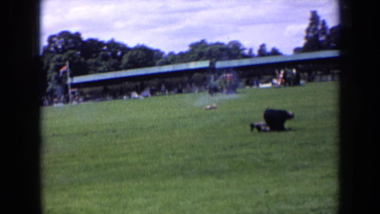 A person on a grass field near a covered pavilion during an outdoor riding event.