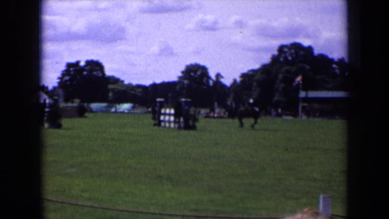 Horse and rider continue across the arena near a striped jump and pavilion.