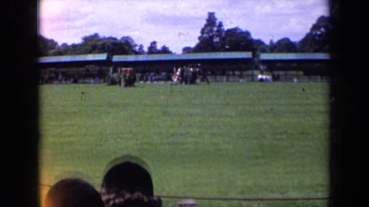 Wide 8mm view from an English equestrian event, showing a horse and rider on grass with a long pavilion and spectators beyond.