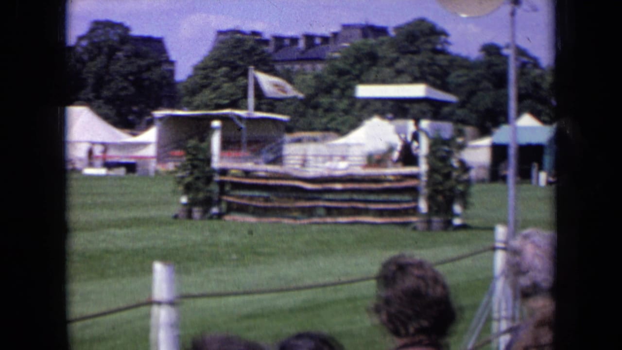1963 England equestrian field with a wooden jump, white tents, rope barrier, and spectators at the edge of the grass.