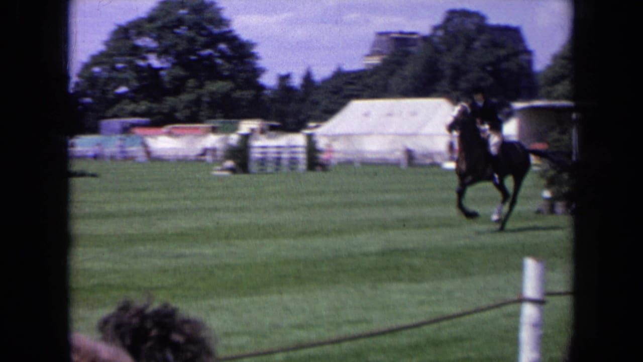 A rider on a dark horse moves across a 1963 England horse-jumping field with tents, trees, and spectators in view.