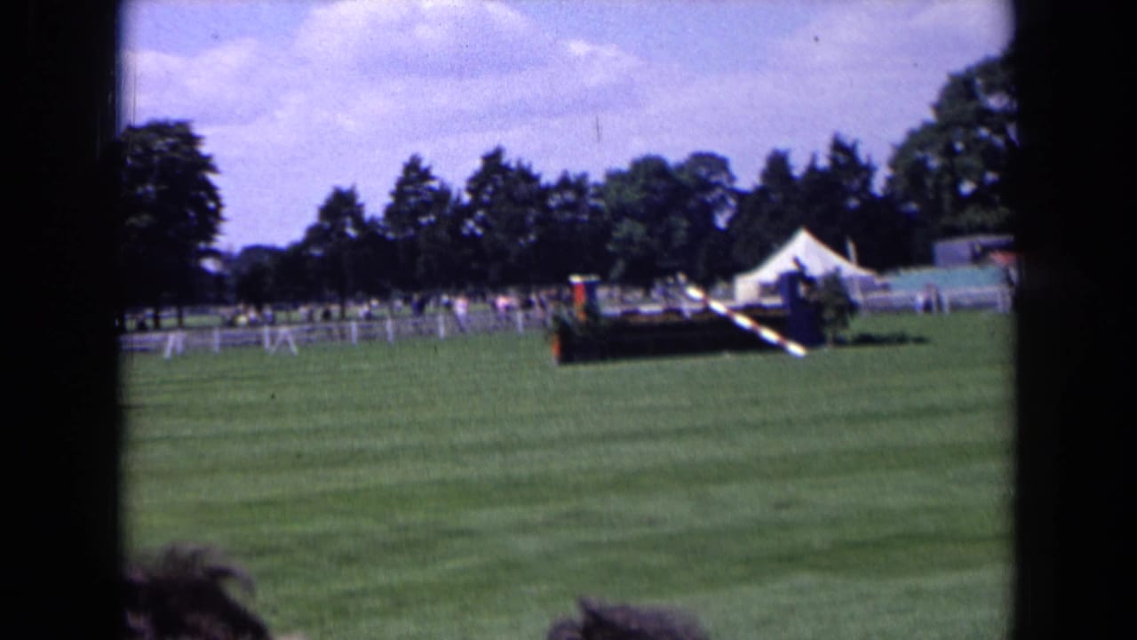 1963 England home-movie view of an equestrian field with a white tent, distant spectators, covered stand, and jump obstacles.
