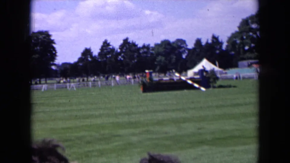 1963 England home-movie view of an equestrian field with a white tent, distant spectators, covered stand, and jump obstacles.