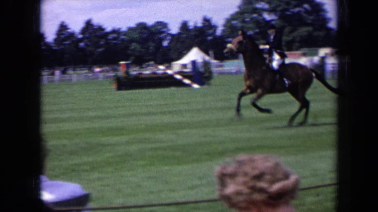 1963 England equestrian footage frame with a rider and brown horse crossing the show field near jumps, tents, trees, and spectators.
