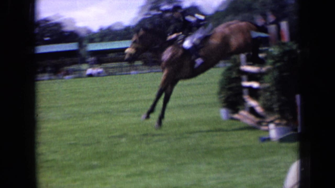 1963 England 8mm frame showing a show-jumping rider and brown horse clearing a wooden obstacle, with motion blur from the jump.