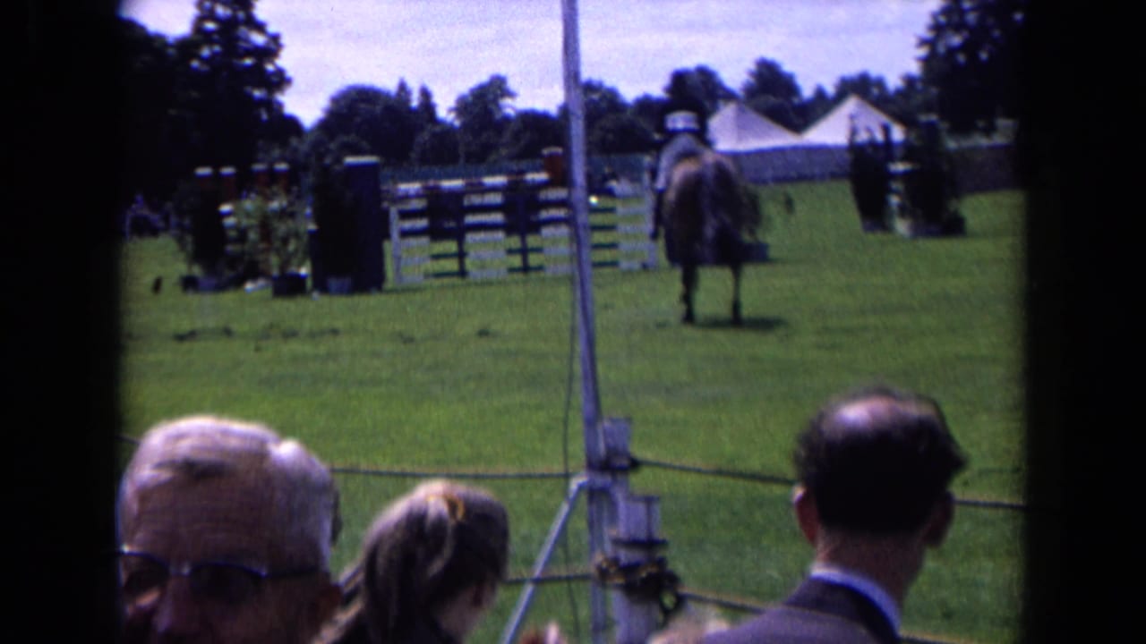 1963 England equestrian-event frame with the horse and rider seen from behind, spectators in the foreground, and jumps across the field.