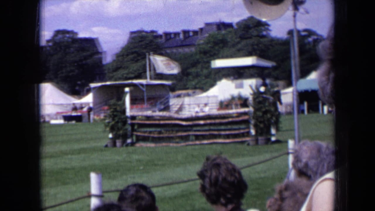 1963 England home-movie view of an equestrian arena, showing the jump area, tents, trees, and watching spectators.