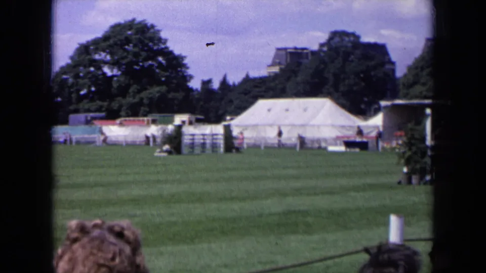 1963 England 8mm frame showing the equestrian field after the horse has moved out of view, with tents and spectators visible.