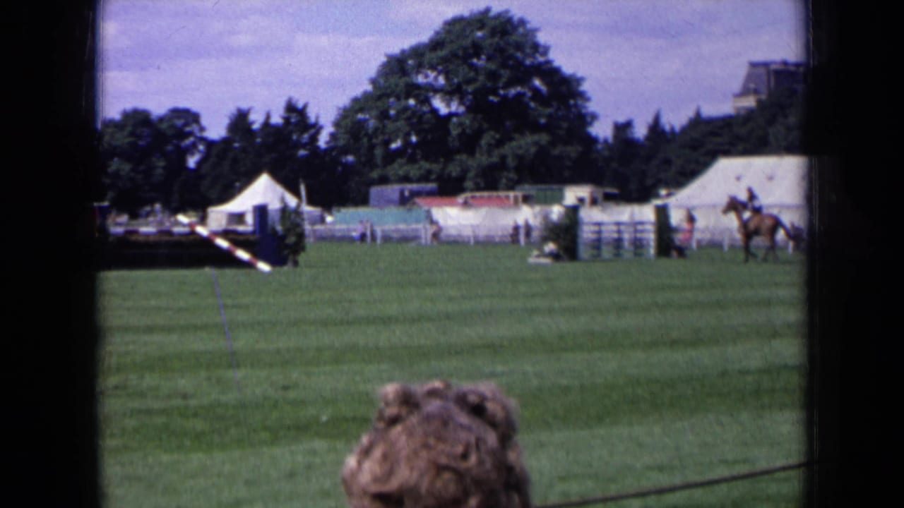 1963 England 8mm view of an equestrian show field with jump rails, white tents, trees, and a foreground spectator.