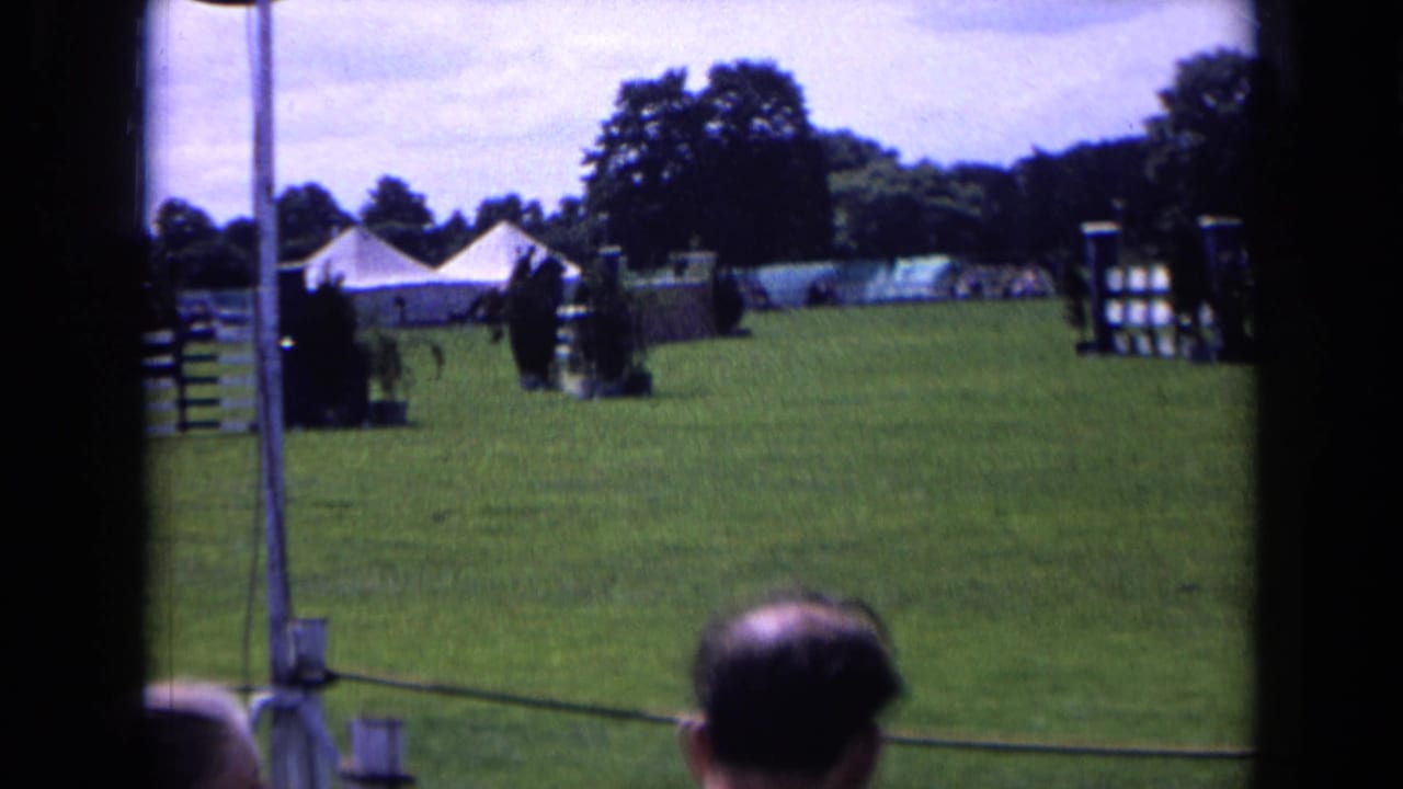 Home-movie view of a 1963 England horse-show arena with jumps, tents, trees, and spectators partly blocking the lower frame.