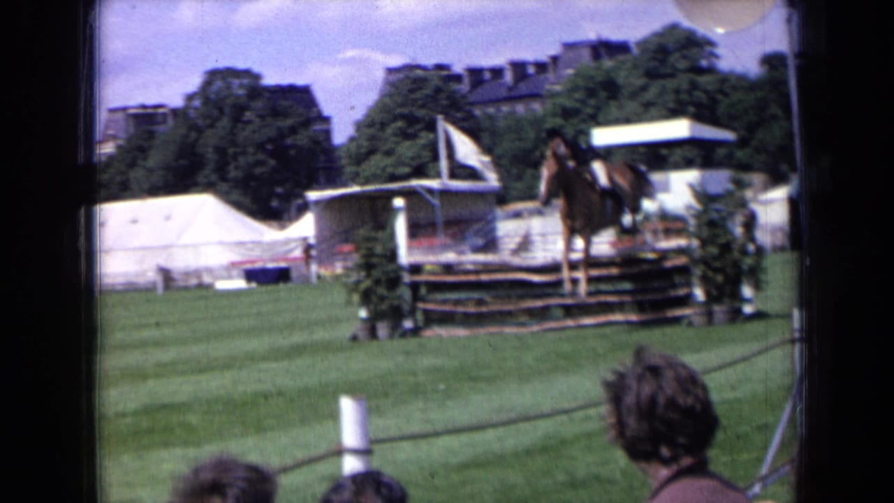 1963 England 8mm frame showing a horse and rider over a wooden show jumping fence, with white tents and spectators nearby.