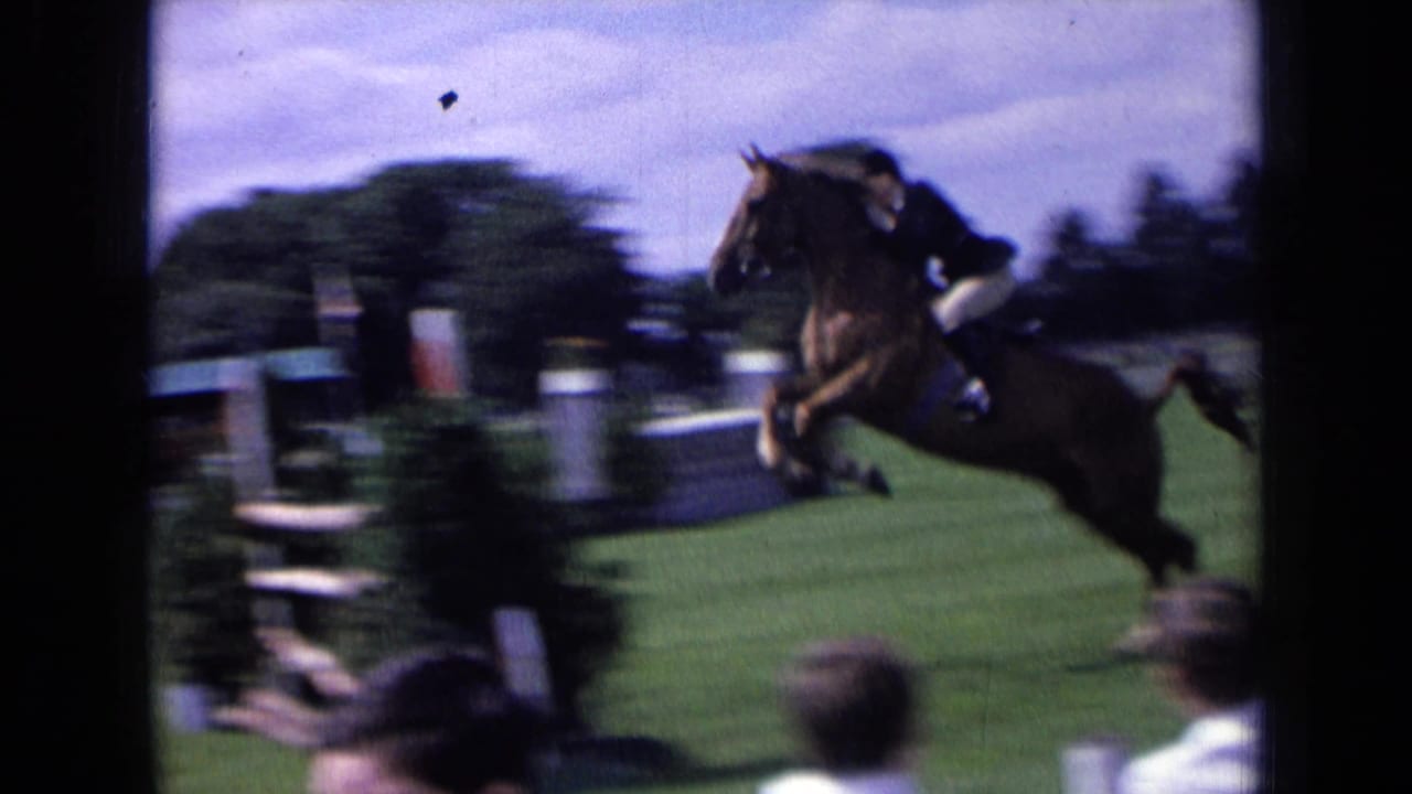 A brown horse with a rider in show attire clears an obstacle on a 1963 England show-jumping field with spectators nearby.