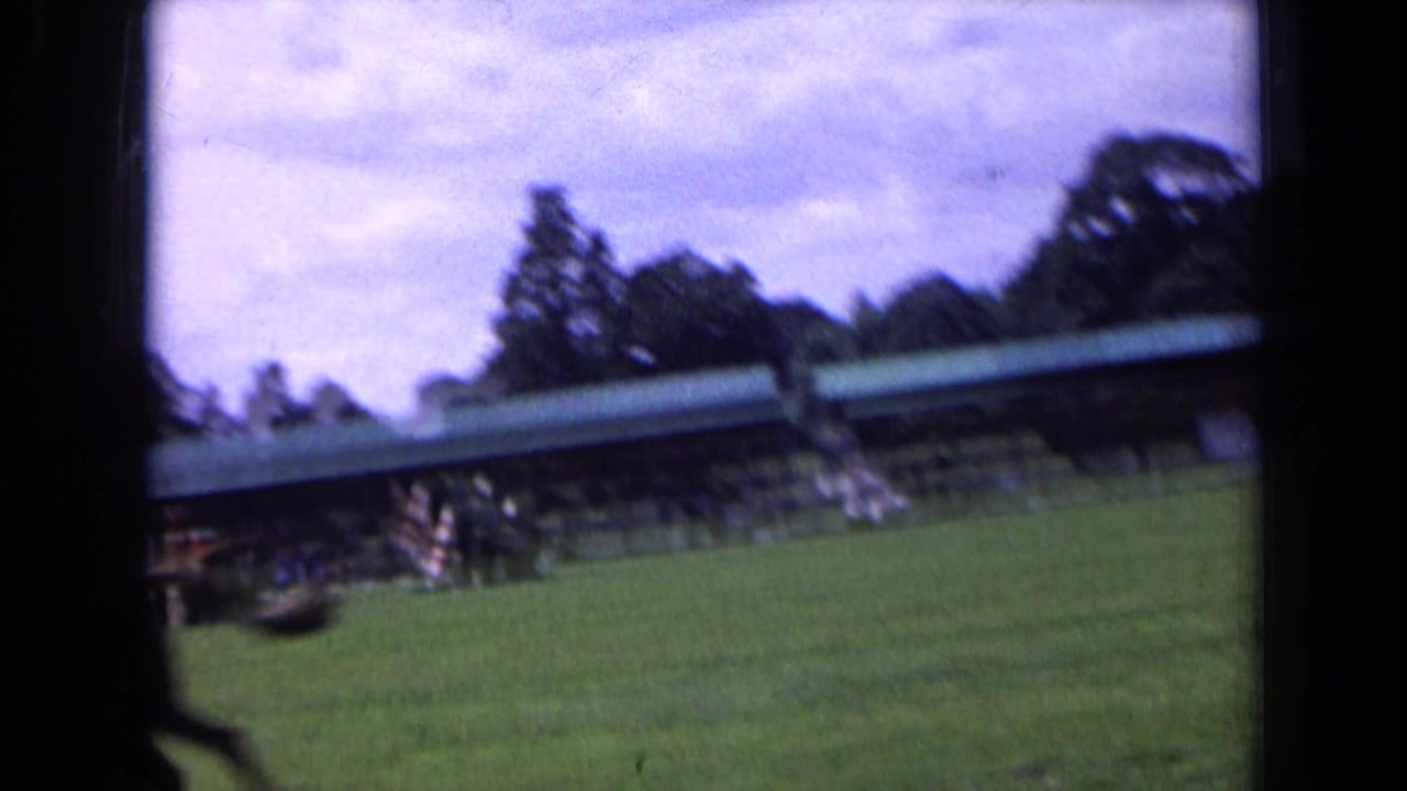 The 8mm camera drifts across the show field, catching a low covered stand, open grass, trees, and blurred spectators in England.
