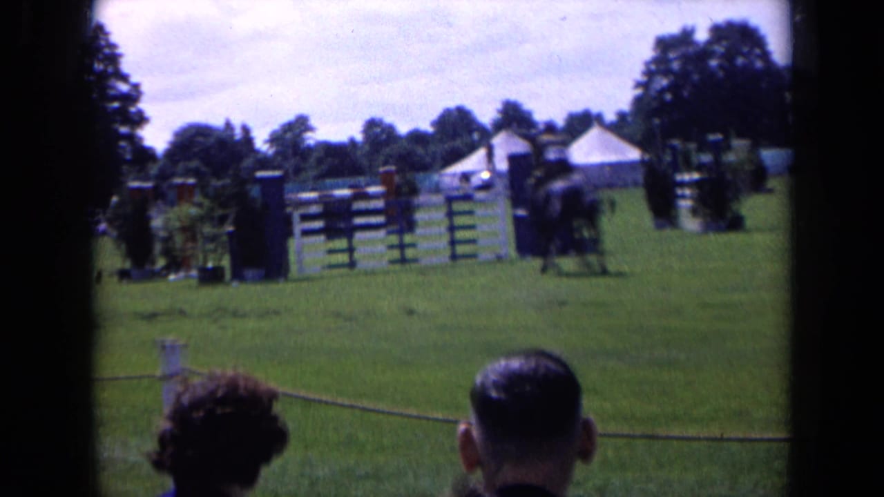 1963 England 8mm view of equestrian jumps on a grass field, with seated or standing spectators in the foreground.