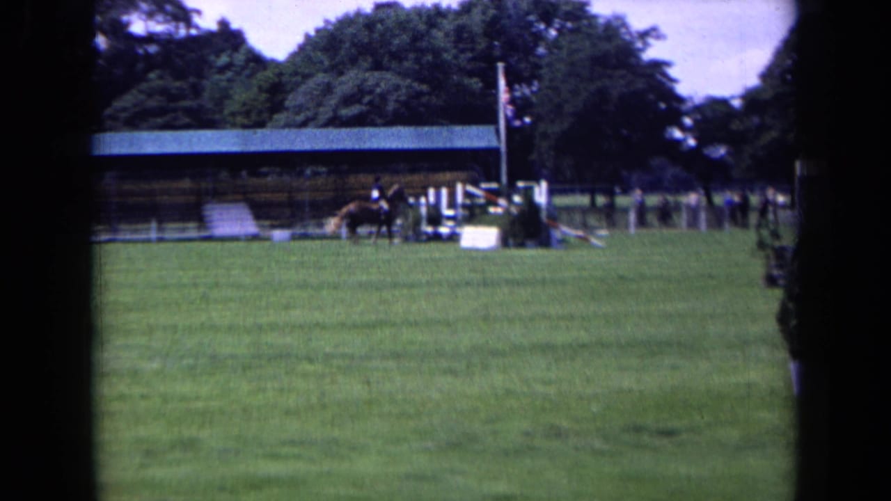 England 1963 frame with a horse and rider near jump obstacles, a covered event structure, trees, and a visible British flag.