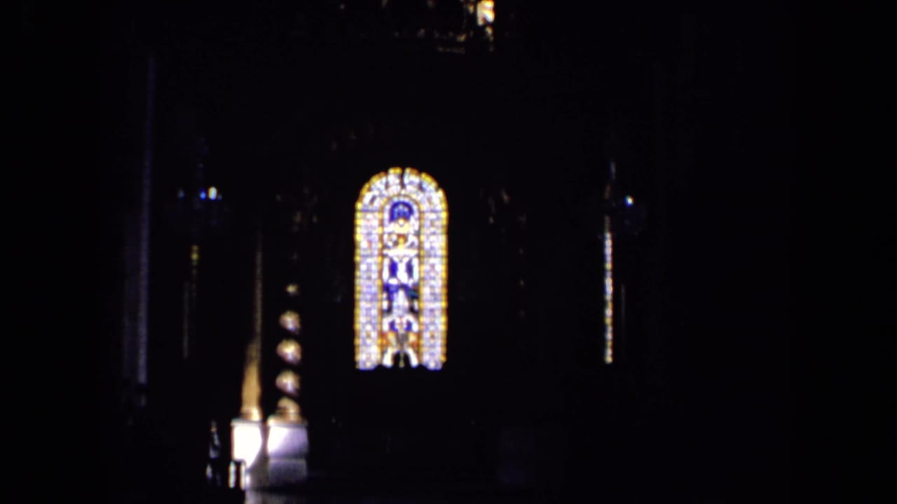 Dark interior frame from the same 1963 England reel, showing a bright stained-glass window and shadowed architectural details.