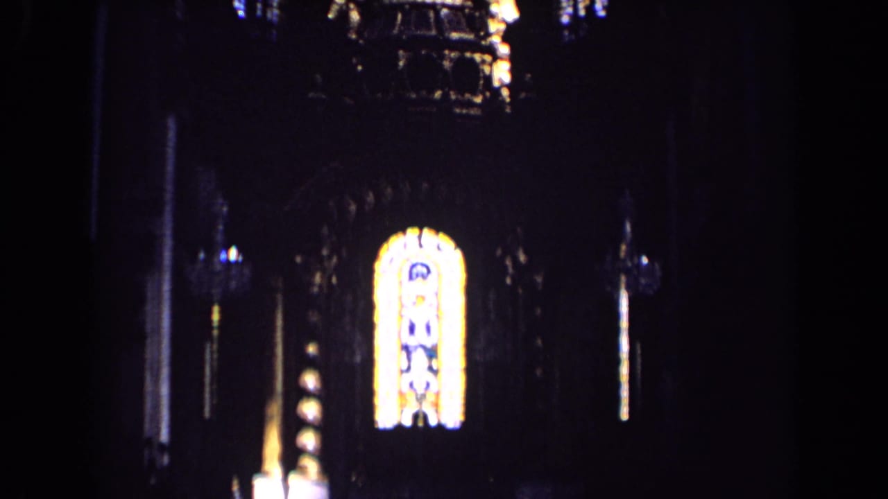 Dark church interior with a glowing stained glass window and shadowed arches.