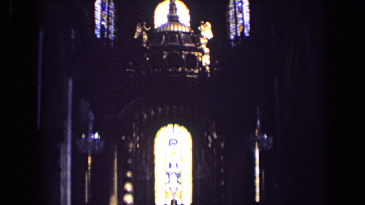 1963 England church interior frame with an ornate central structure, angel statues, and glowing stained glass above.