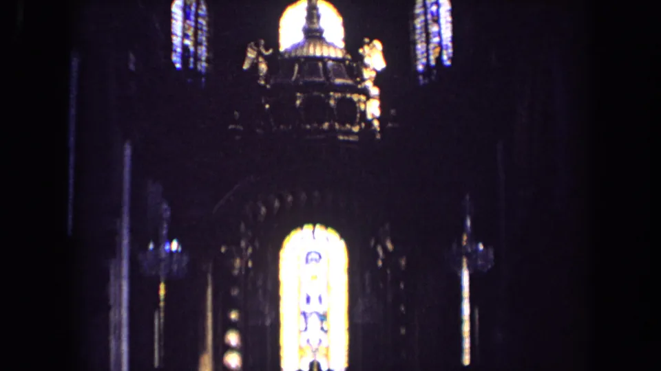 1963 England church interior frame with an ornate central structure, angel statues, and glowing stained glass above.