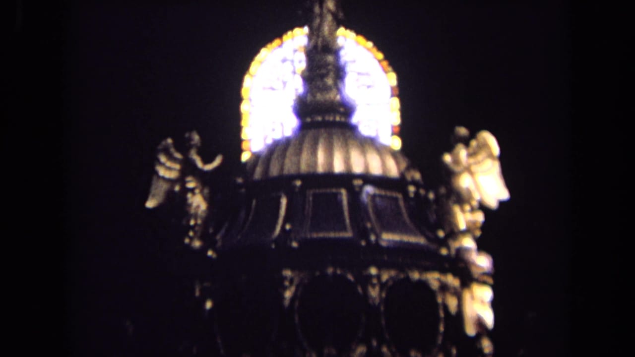 1963 England 8mm frame showing a dark church interior detail with gilded angel statues and glowing stained glass behind a domed canopy.