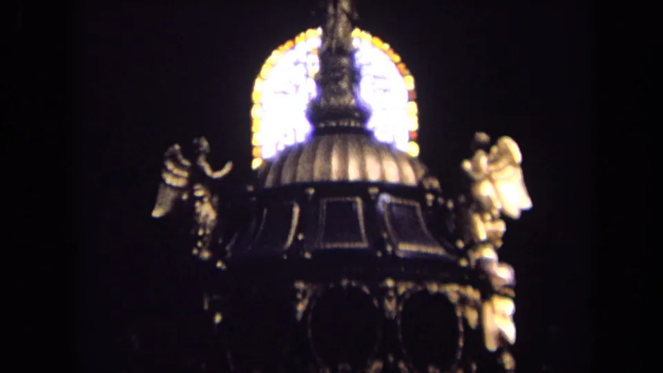 1963 England 8mm frame showing a dark church interior detail with gilded angel statues and glowing stained glass behind a domed canopy.