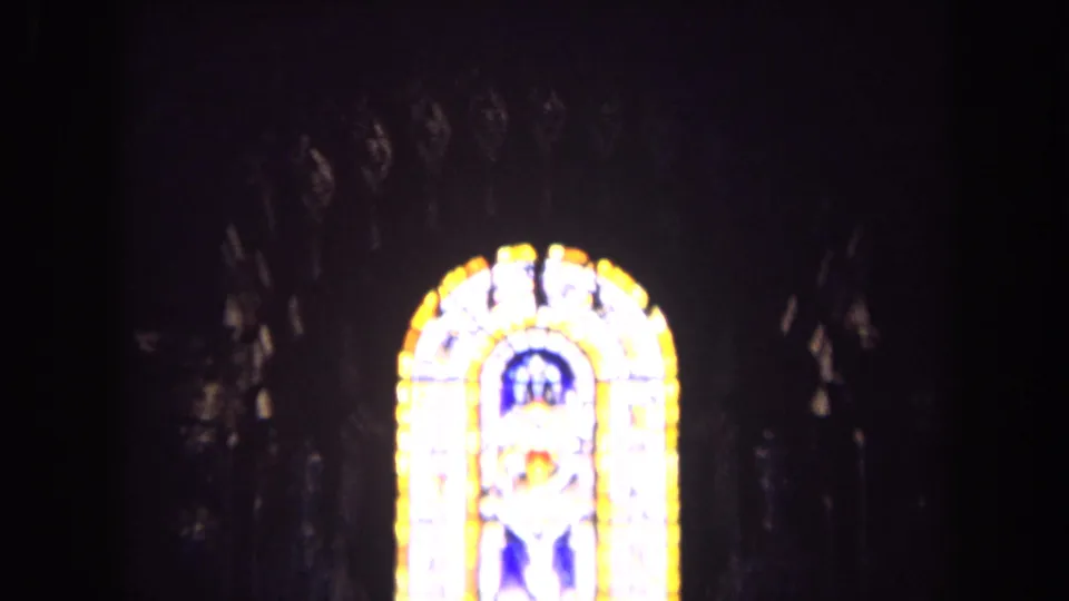 1963 England 8mm frame of a bright stained glass window glowing against the dark interior of a church.