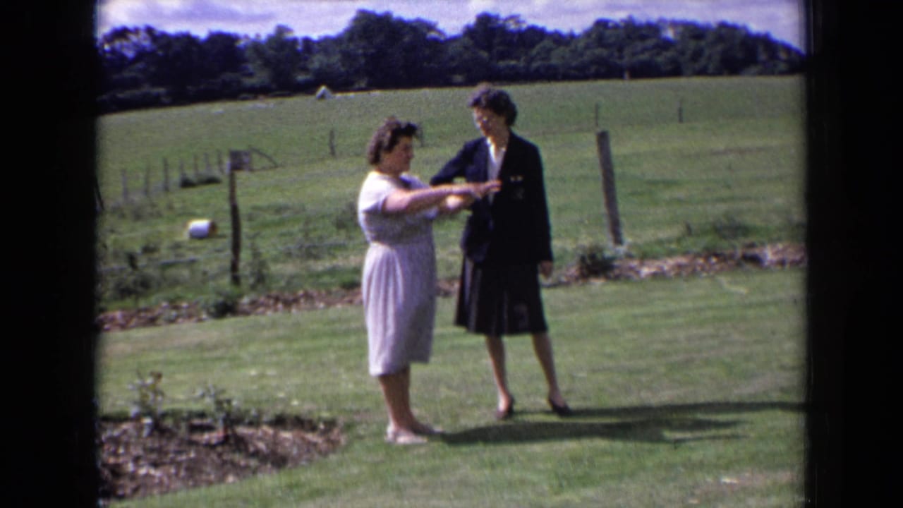 A woman gestures with both hands while another woman watches on the lawn.
