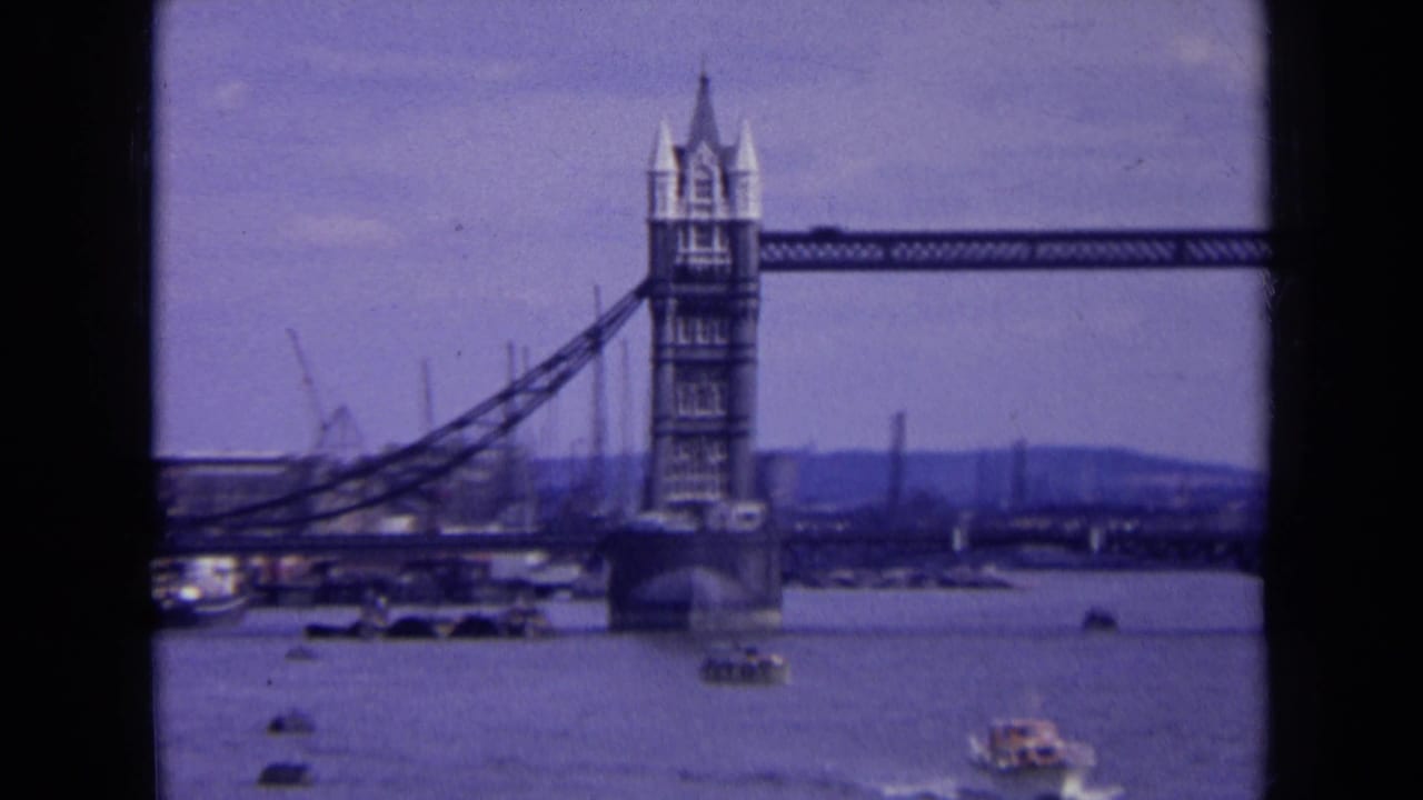 1963 London 8mm frame showing Tower Bridge over the River Thames with small boats and a hazy industrial shoreline beyond.