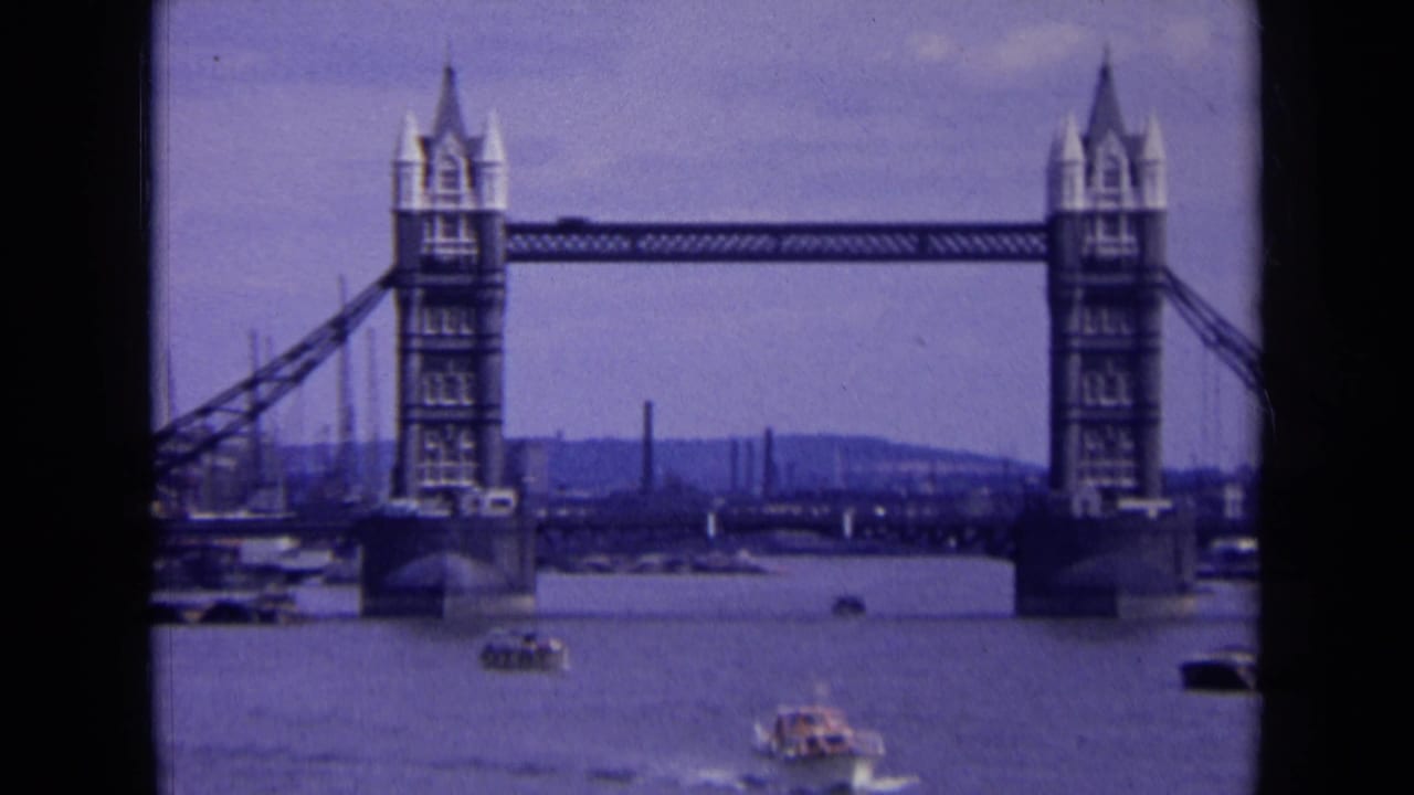 1963 London home-movie frame of Tower Bridge across the Thames, with small boats moving below and industrial details behind it.