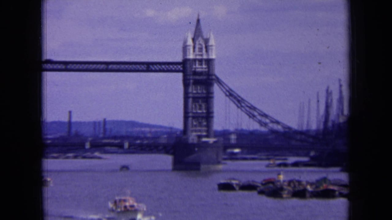 1963 London 8mm frame with one Tower Bridge tower prominent, the Thames below, and cranes or moored craft along the right side.