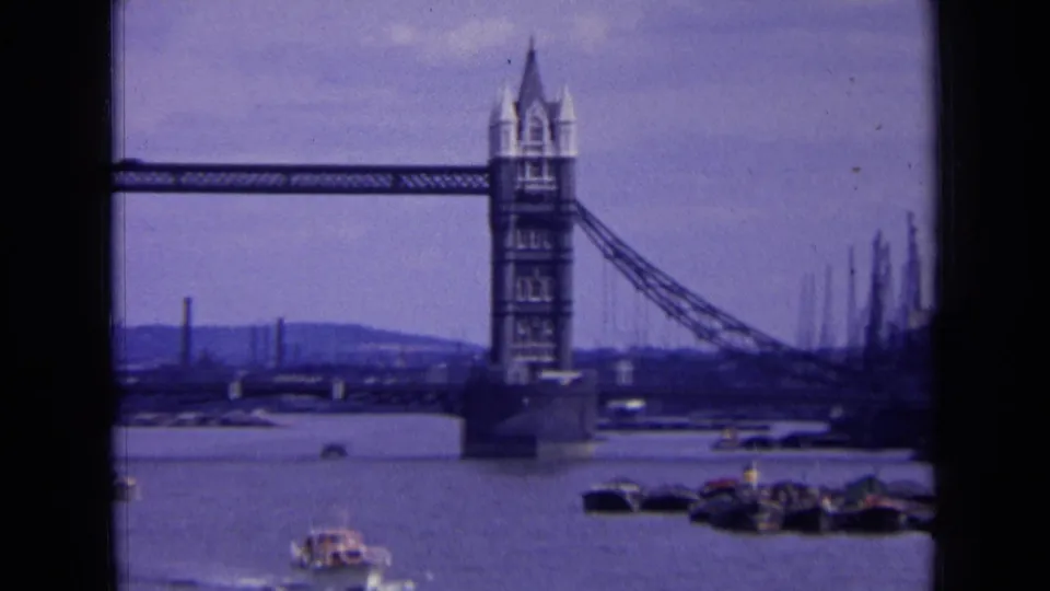 1963 London 8mm frame with one Tower Bridge tower prominent, the Thames below, and cranes or moored craft along the right side.