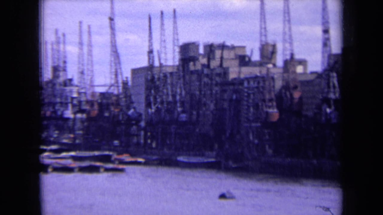 1963 England frame of dockside cranes and industrial buildings lining the river, with small craft near the waterfront.